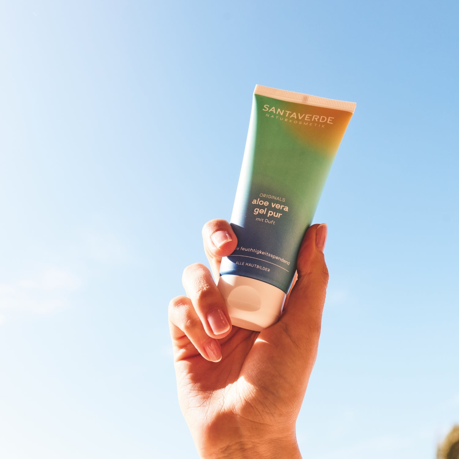Santaverde aloe vera gel pur mit Duft in der Hand in den blauen Himmel gehalten